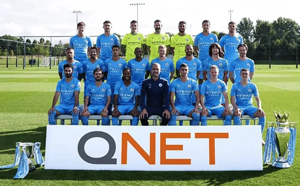 football players taking a photo in front of QNET logo on football pitch
