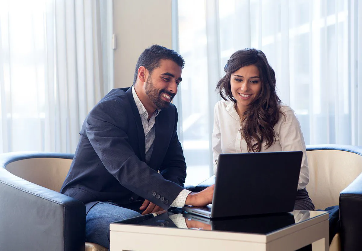 man and woman sitting at computer smiling working
